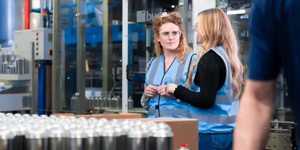 Twee Personen Van Nrg Office Praten Met Elkaar In Een Supply Chain Omgeving Met Veiligheidshesjes Aan